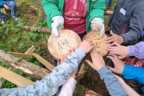 Eine nassen und eine trockene Holzscheibe wird von Kindern mit den Händen nach Gewicht verglichen